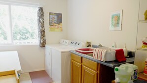 A laundry room with a washing machine, dryer, and a sink with a red towel. There is a window with curtains and a poster on the wall.