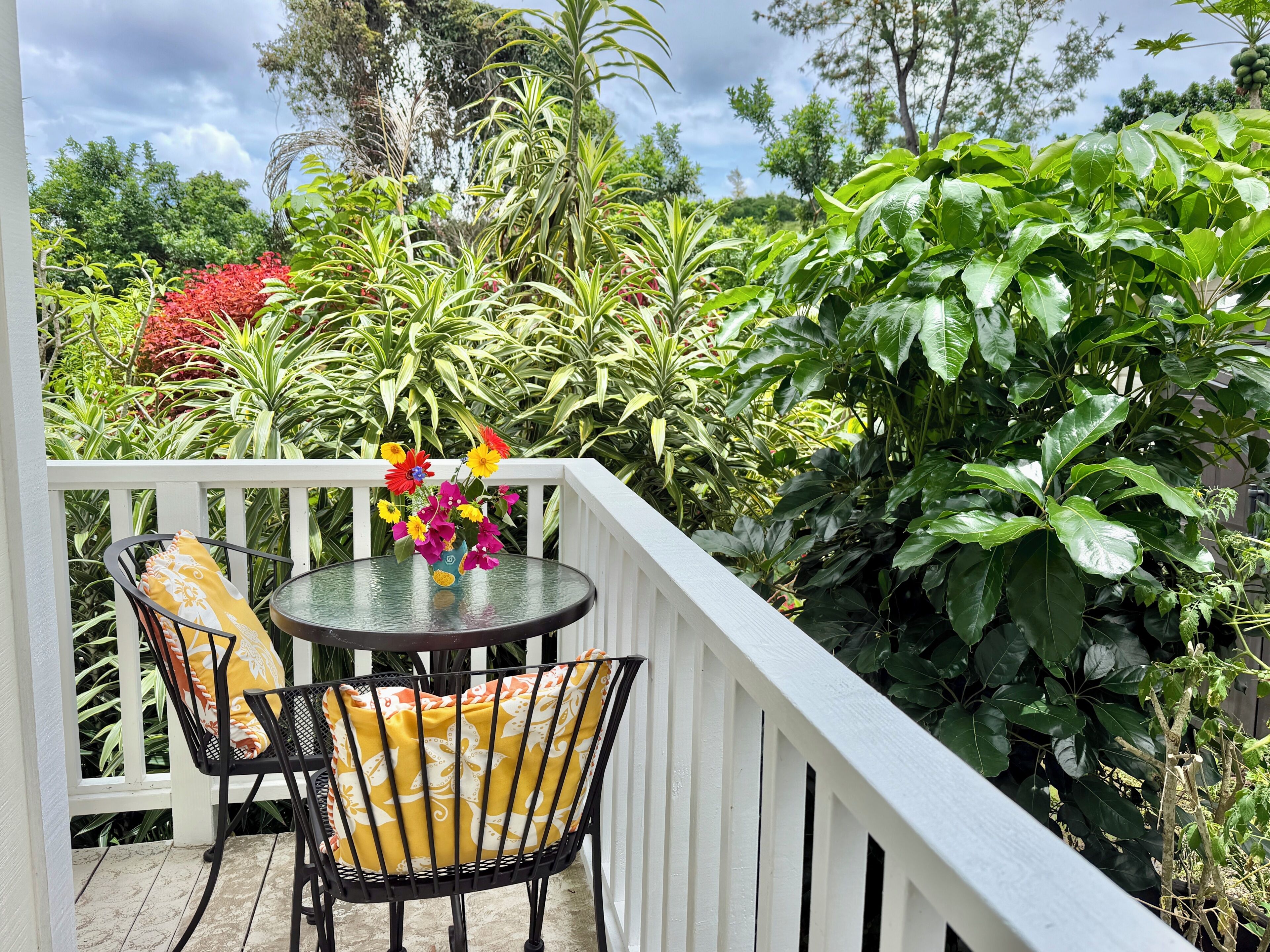 A balcony with a table and chairs, surrounded by lush greenery and a white railing.