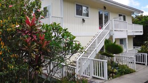A two-story building with a white exterior, a balcony on the second floor, and a staircase leading to the entrance.