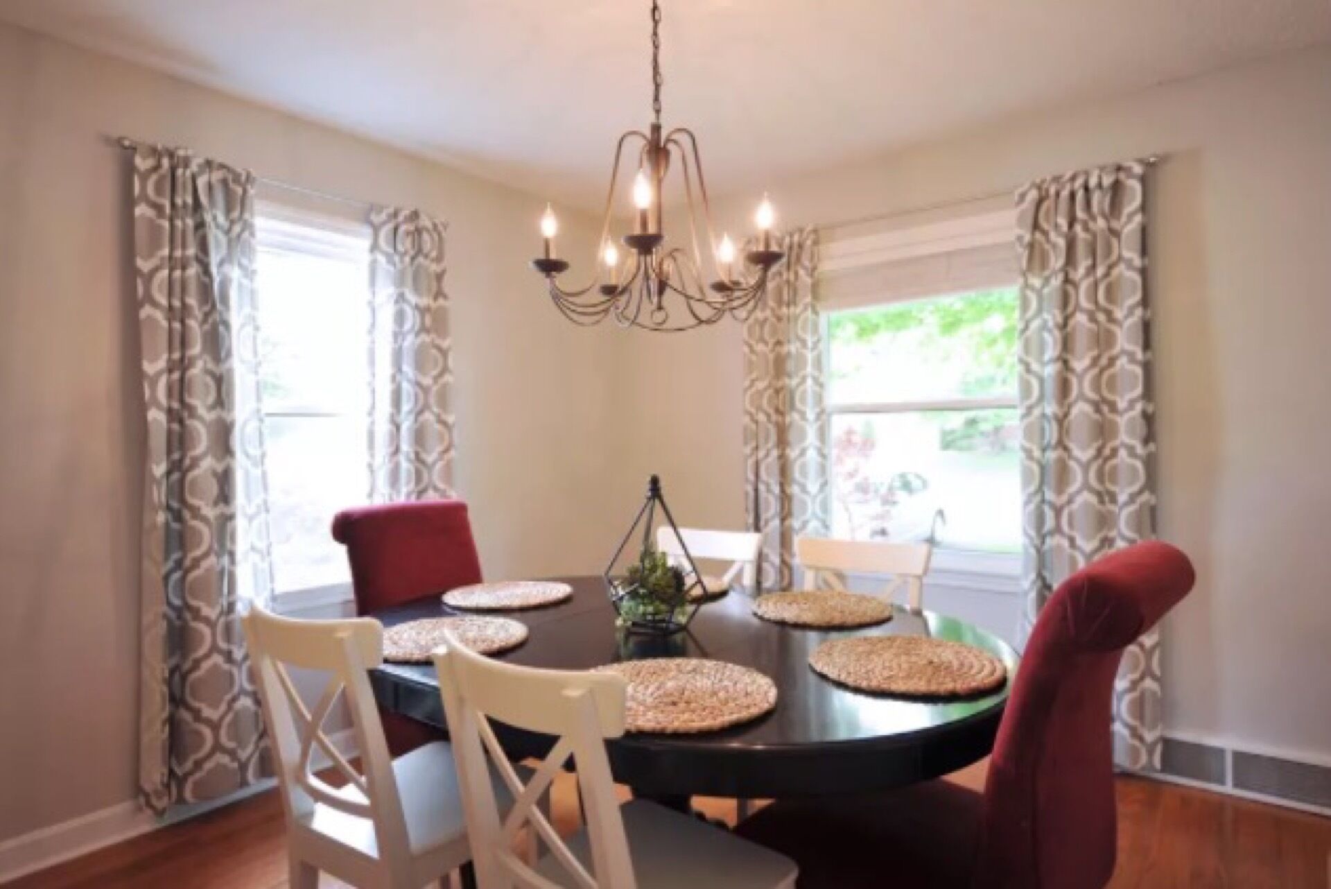 A dining area with a round table, four chairs, a chandelier, and patterned curtains.