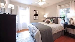 Un dormitorio con cama, ventilador de techo, cómoda y ventana con cortinas.