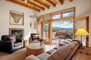 A spacious living room with a fireplace, leather sofas, a round coffee table, and large windows offering a view of the landscape.