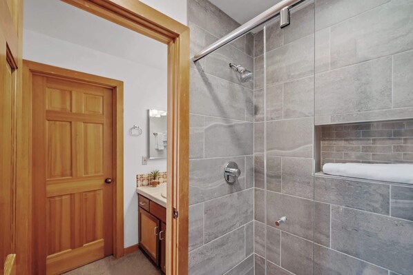 A bathroom with a shower, a wooden door, and a vanity with a mirror and sink.