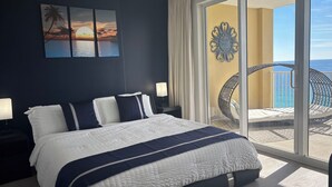 Un dormitorio con una cama grande, un ventilador de techo y vistas al océano a través de un cristalero corredizo.