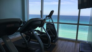 Un gimnasio con cintas de correr y una máquina elíptica, ventanas amplias con vista al océano.