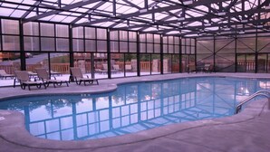 Ein überdachter Innenpool mit Panoramafenstern, umgeben von Liegestühlen und einer Terrasse.