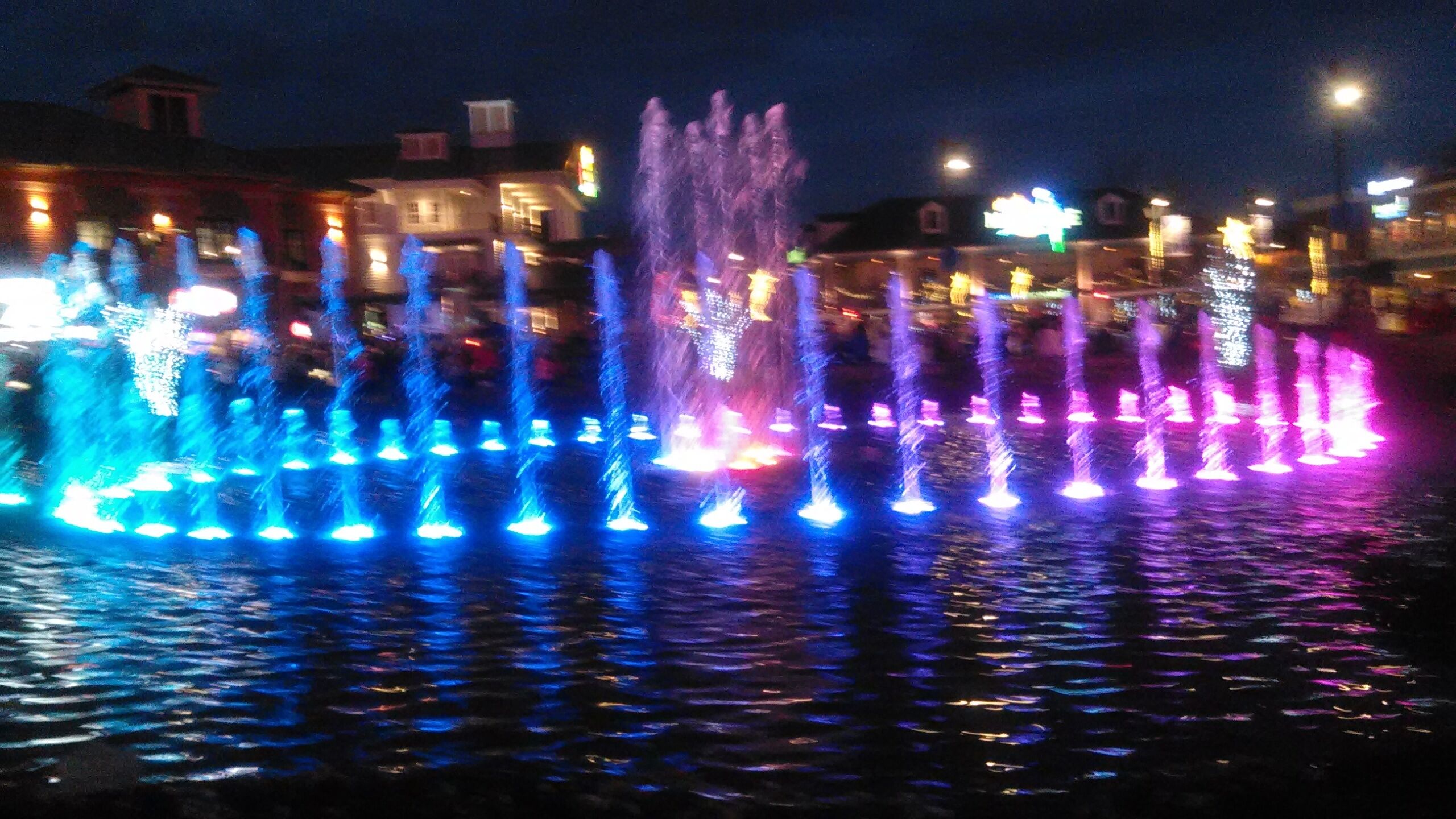 A nighttime fountain with multiple water jets illuminated in various colors.