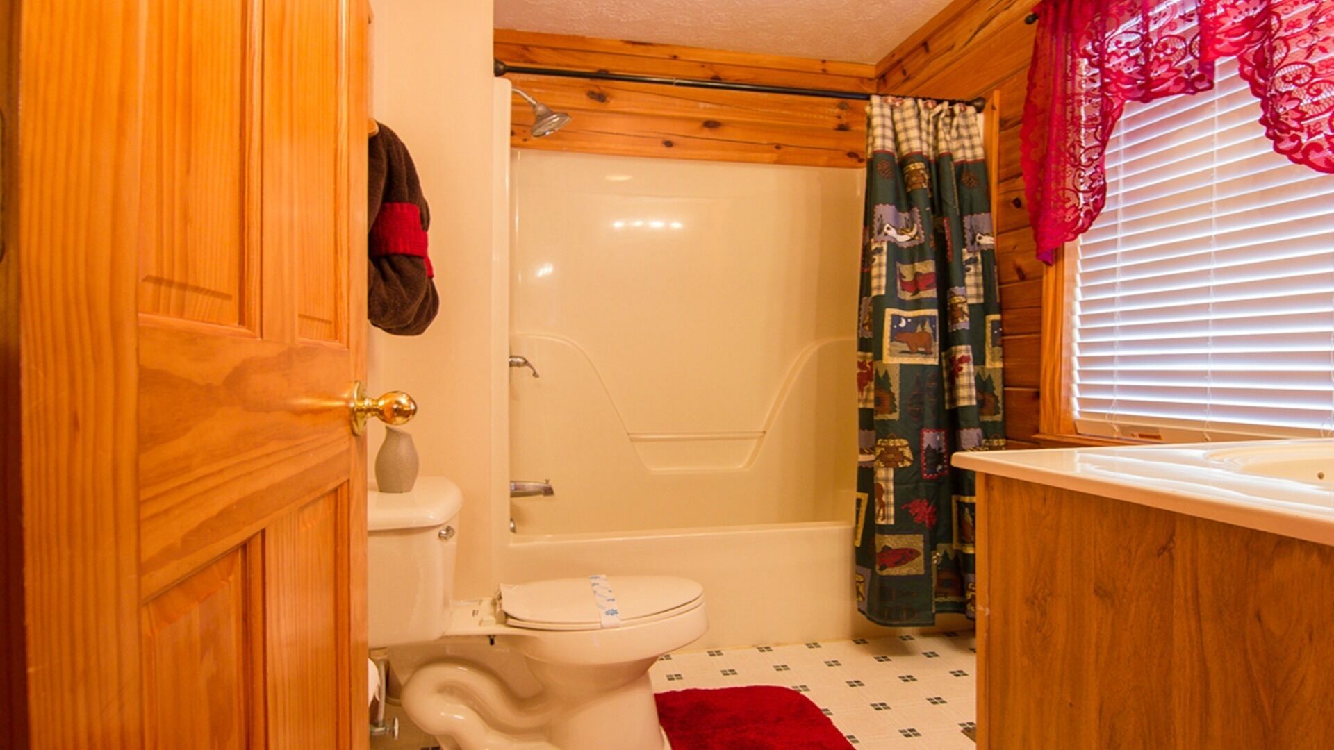 Un baño de madera con inodoro, ducha y una ventana con persianas.