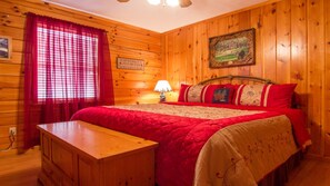 Quarto de cabana de madeira com uma cama, uma mesinha de cabeceira e uma janela com cortinas vermelhas.