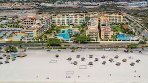 A resort with multiple buildings, a large pool, and a beach with umbrellas.