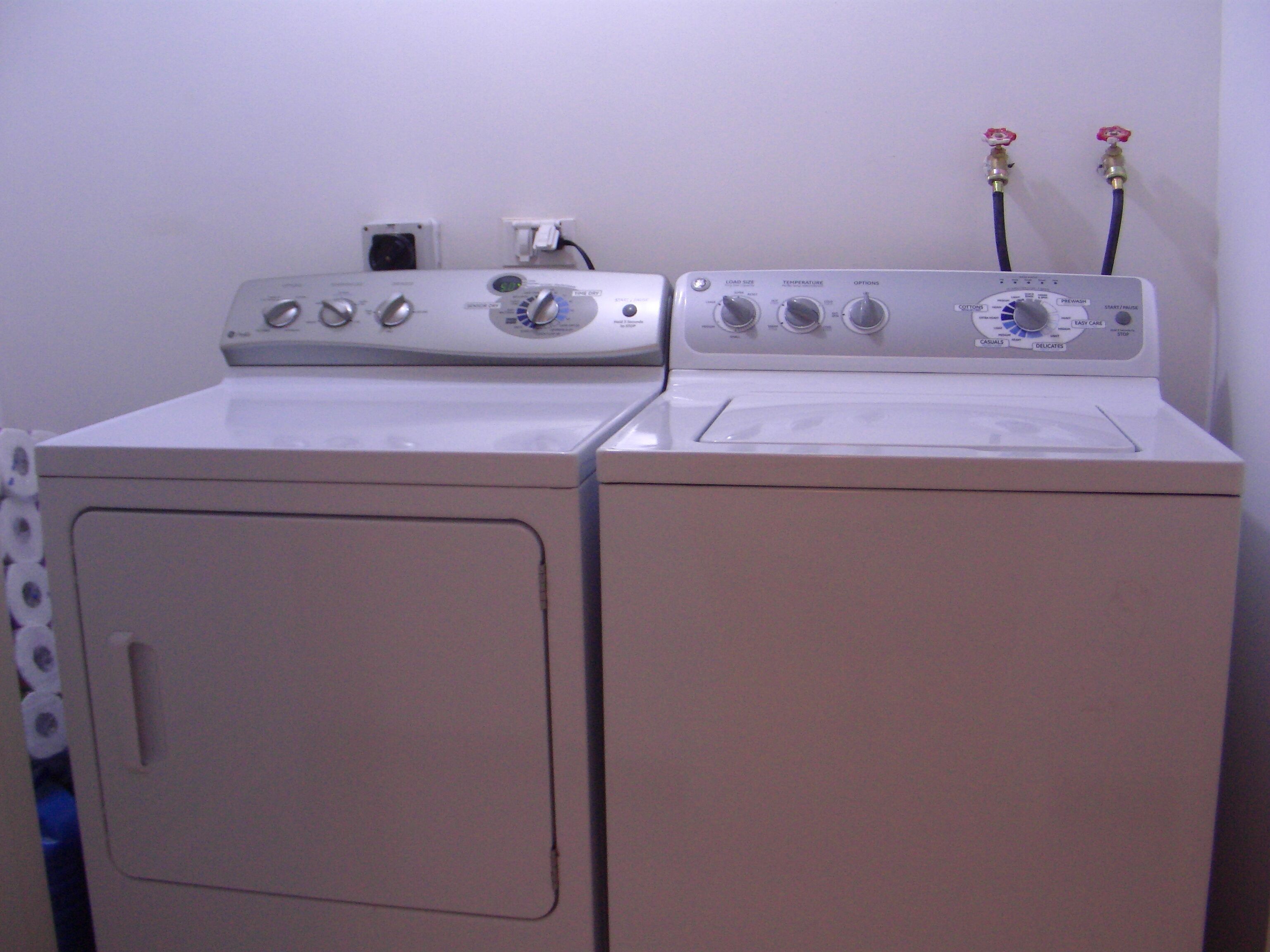 Un appareil combiné lave-linge et sèche-linge à chargement frontal, doté de boutons de commande et de tuyaux.