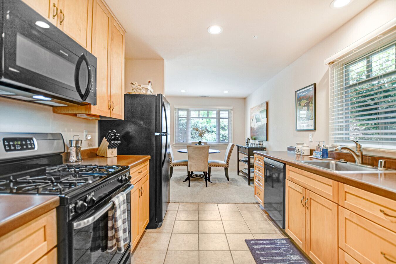 A kitchen with wooden cabinets, a black refrigerator, a stove, and a dining area with a chair and table.