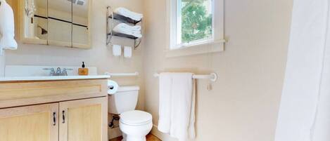 Un baño moderno con tocador de madera, inodoro blanco, toallero y ventana que proporciona luz natural.