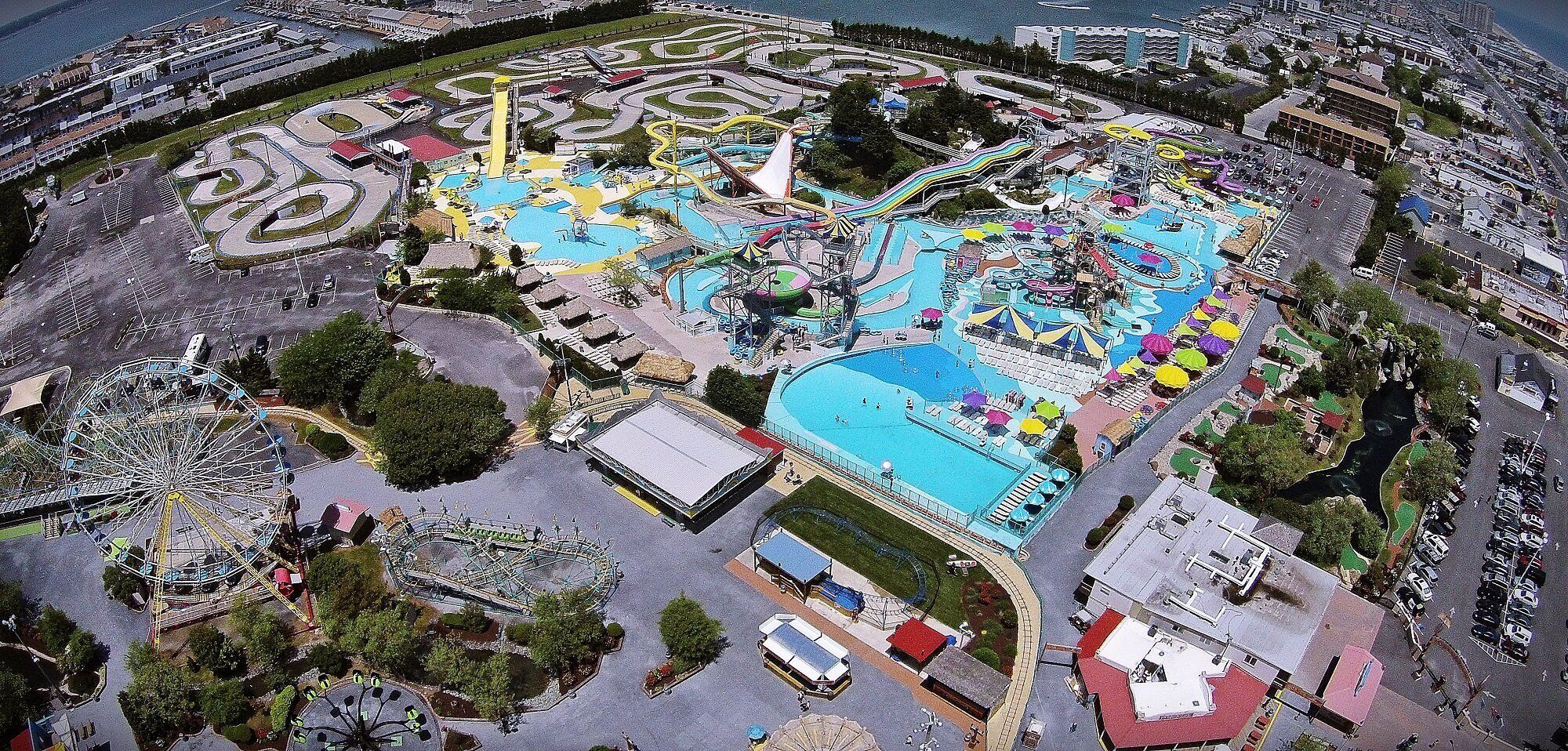 Vue aérienne d’un parc d’attractions comprenant un grand parc aquatique, une grande roue et diverses attractions.