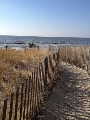 Een zandpad dat naar het strand leidt, omzoomd door een houten hek en droog gras.