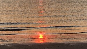 Auringonlasku tyynen meren yllä, edessä hiekkaranta.