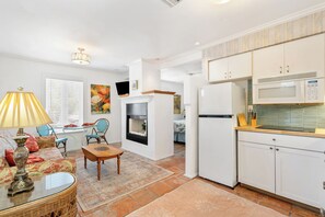 A living room with a fireplace, a dining area, and a kitchen with white cabinets and a microwave.