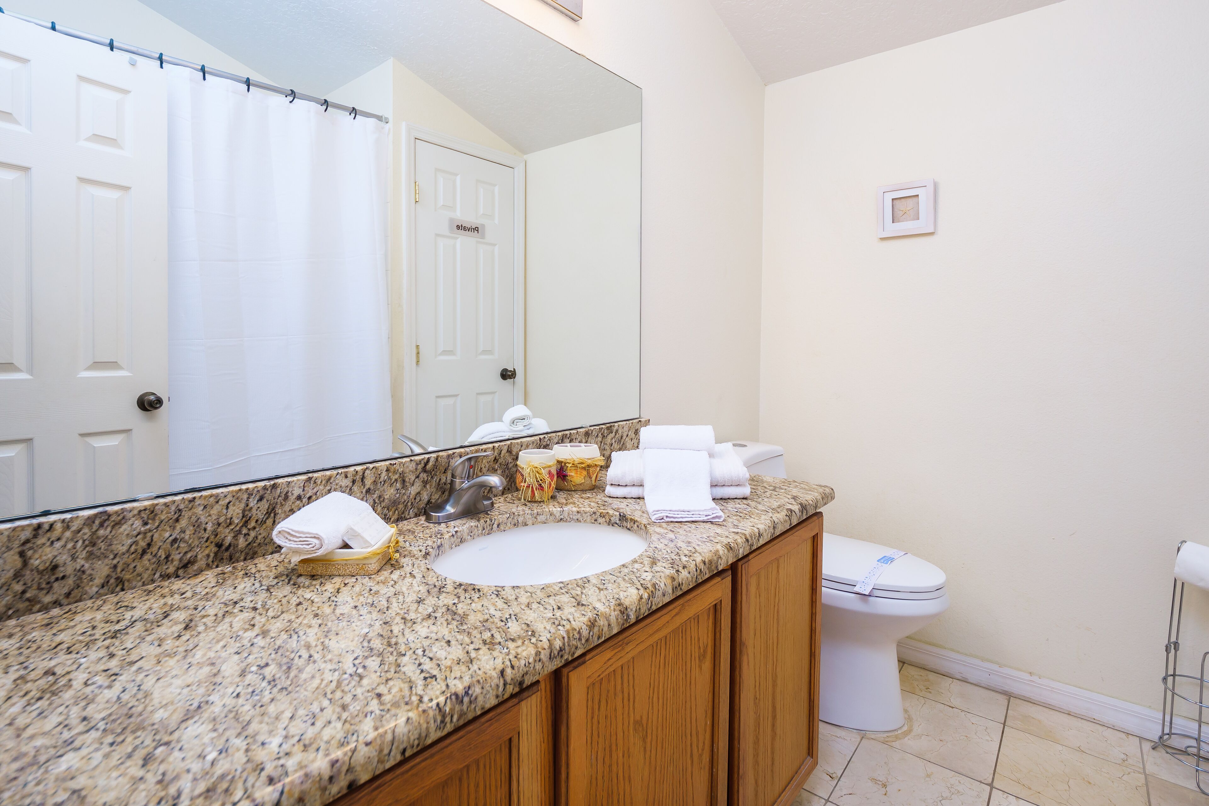 Une salle de bain avec un comptoir en granit, un lavabo, des toilettes et un grand miroir.