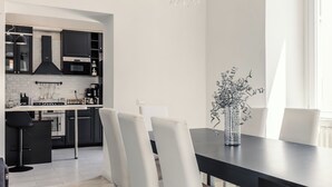 Une cuisine moderne avec des meubles noirs, un plan de travail blanc et un coin repas comprenant des chaises blanches et une table foncée.
