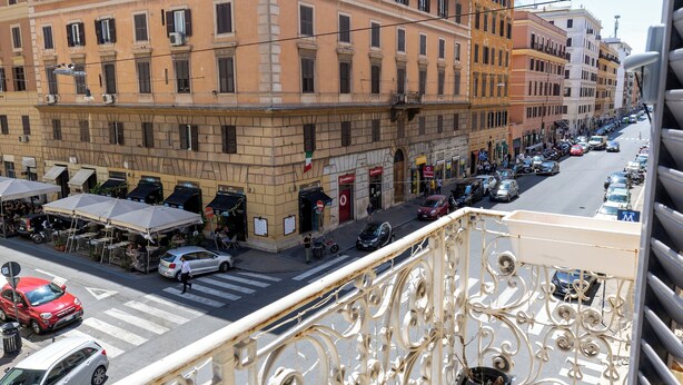 Un balcon orné de balustrades en métal ouvragé, donnant sur une rue bordée de voitures garées et d’immeubles.