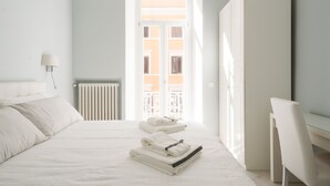 Une chambre d’hôtel avec un lit, une chaise, un radiateur et une fenêtre donnant sur un immeuble.