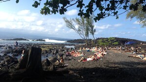 Una playa con gente tomando el sol y nadando, rodeada de terreno rocoso y árboles.
