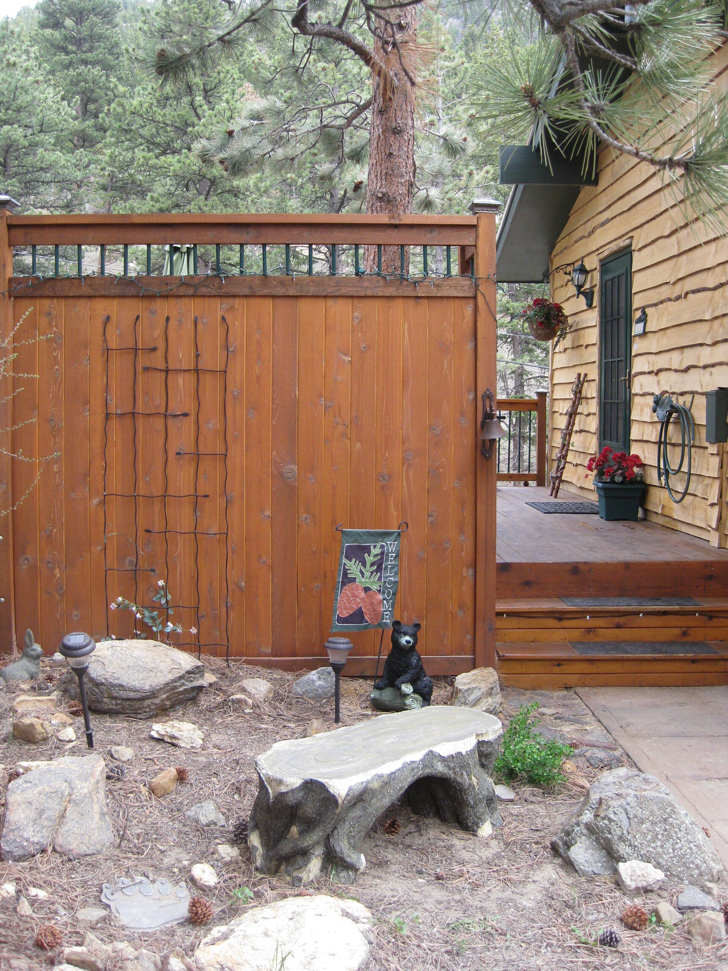 A wooden fence with a welcome sign, a bear statue, and a stone bench in a garden area.