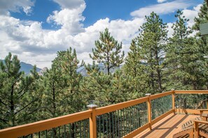 A wooden deck with a metal railing overlooking a forest of pine trees and distant mountains. - Pine Cone Cabin, Walk to Town, Private Location, Hot Tub, Wood FP (Estes Park)