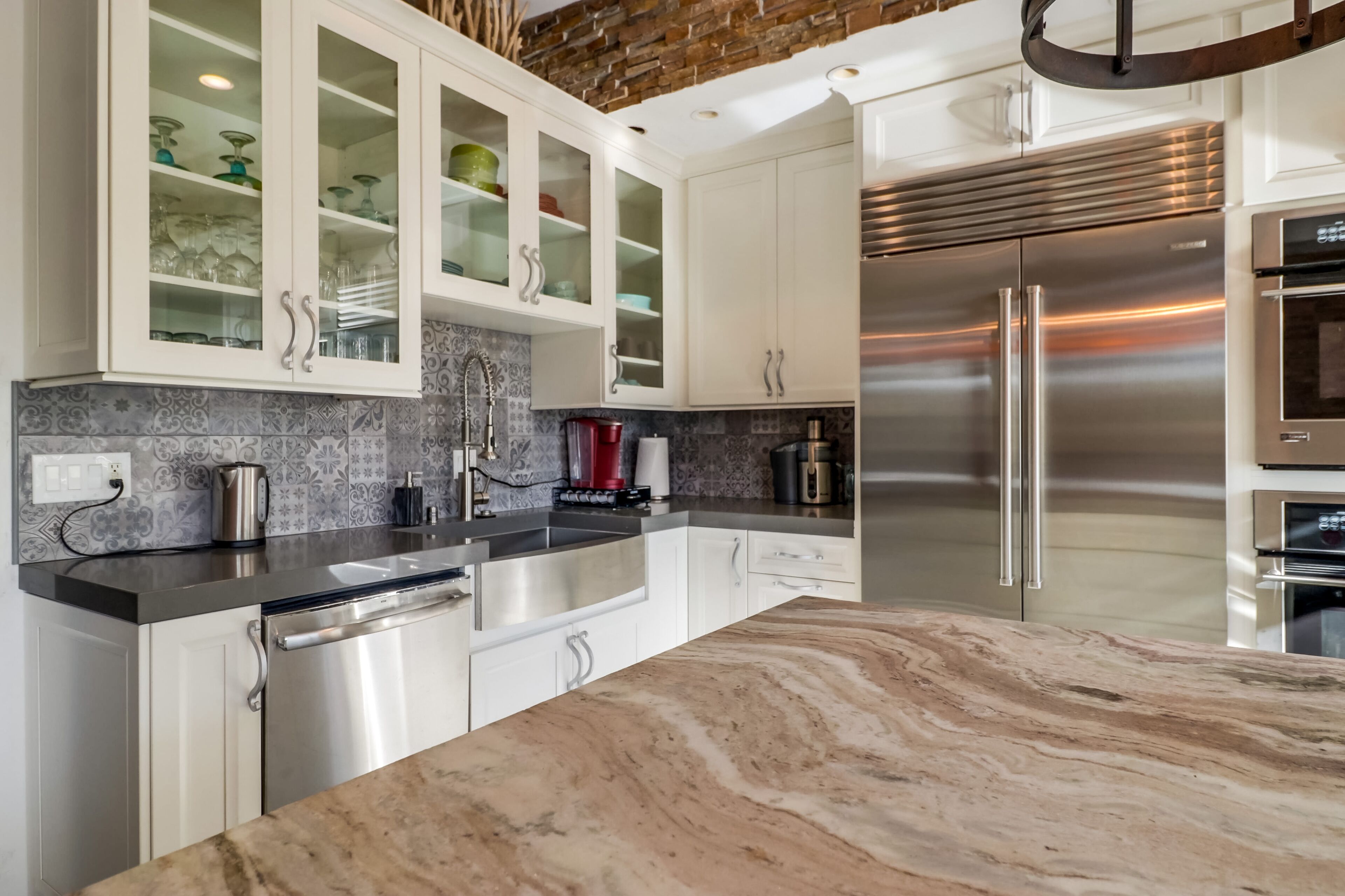 A modern kitchen with white cabinets, a stainless steel refrigerator, and a marble countertop.
