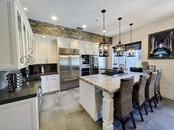 A modern kitchen with white cabinetry, stainless steel appliances, a central island with bar seating, and a stone accent wall.