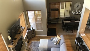 A spacious living room with a grey sectional sofa, a stone fireplace, and a dining area with a table and chairs.