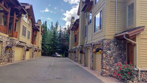 A row of two-story buildings with stone foundations and wooden balconies, a paved street, and a car parked in the distance.