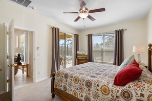 Un dormitorio con cama, ventilador de techo, ventana con cortinas y vista al exterior.