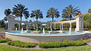 A fountain with multiple water jets, surrounded by palm trees and a white gazebo structure.