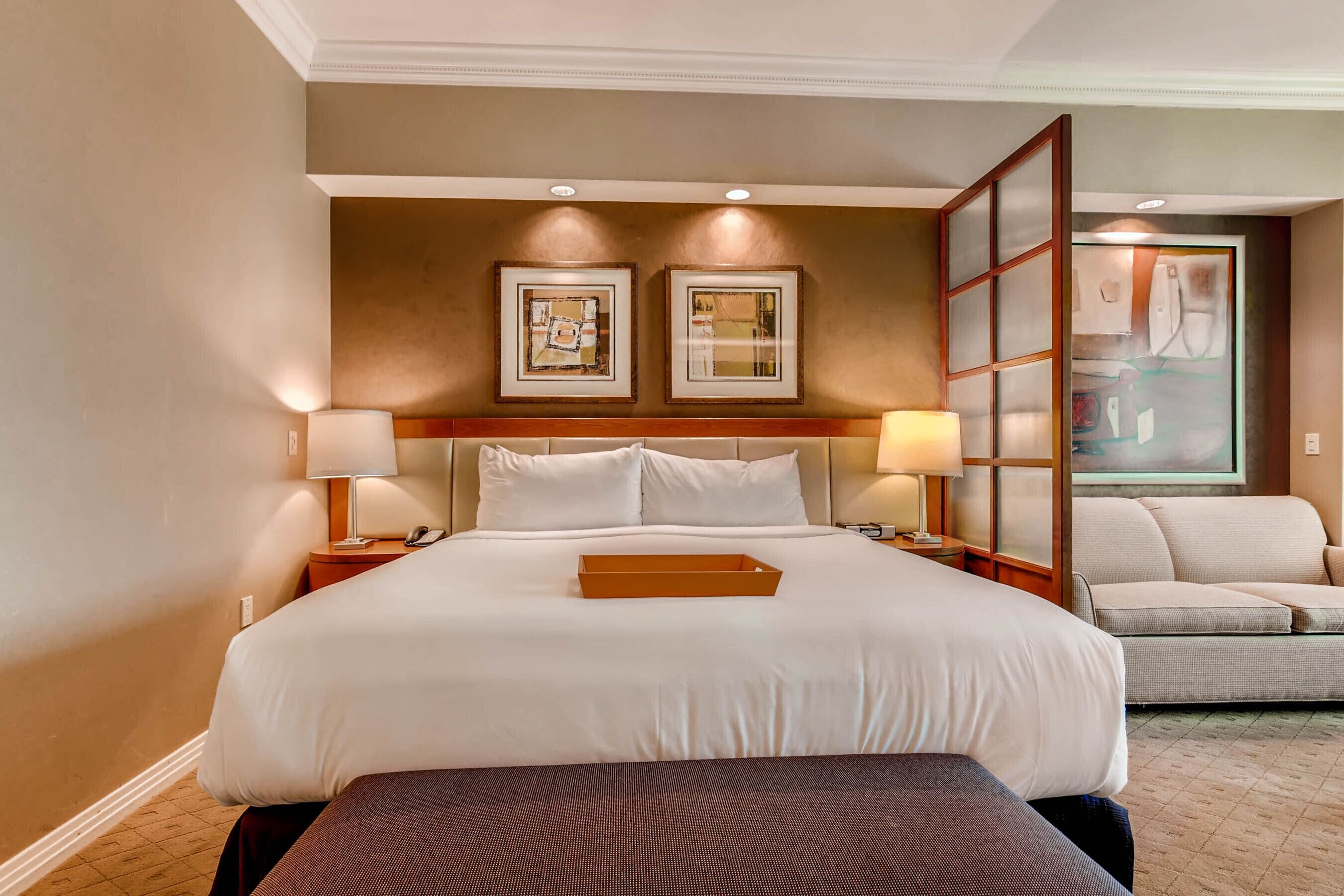 Une chambre d’hôtel avec un grand lit, deux tables de chevet avec des lampes, un canapé et deux œuvres d’art encadrées accrochées au mur.