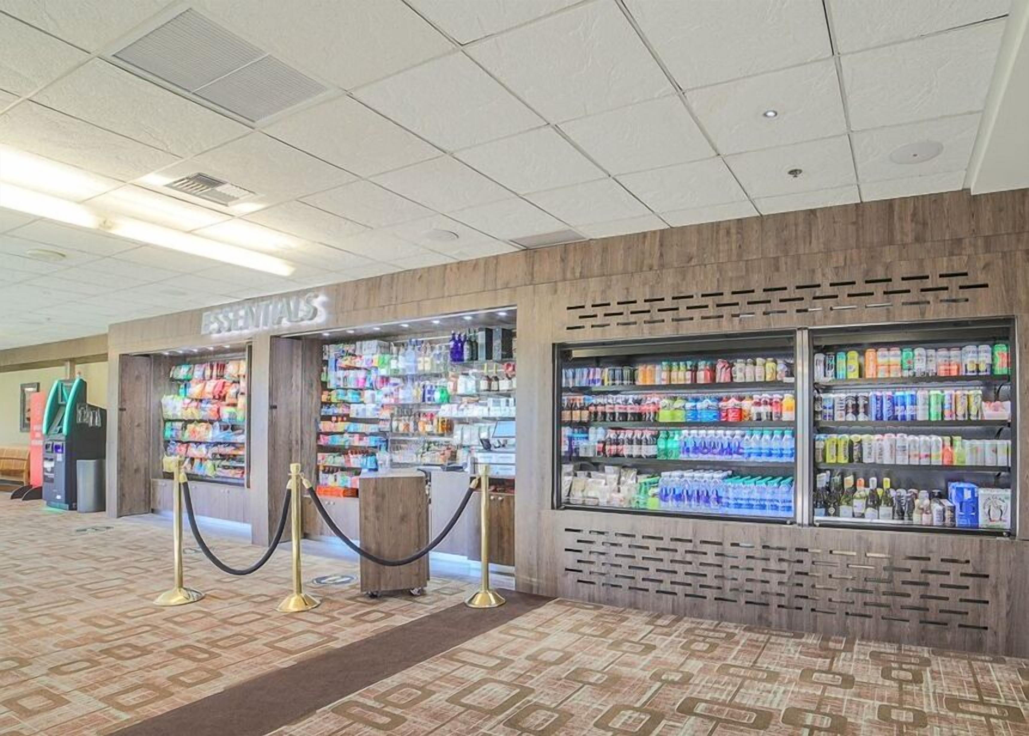 Un espace commercial proposant une variété de produits, notamment des collations et des boissons, et dont l’entrée, bien visible, mène à un magasin appelé « ESSENTIALS ».