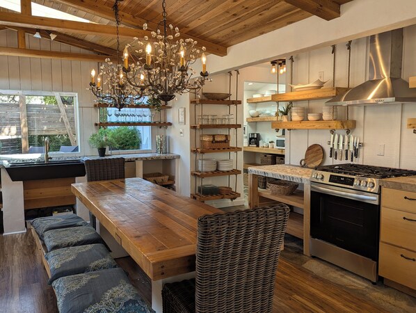 A kitchen with a wooden table, wicker chairs, a chandelier, and a stove.