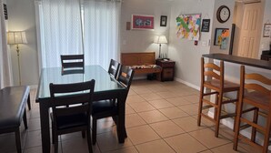 A dining area with a glass table and wooden chairs, a ceiling fan, a lamp, and a wall with various notes and pictures.