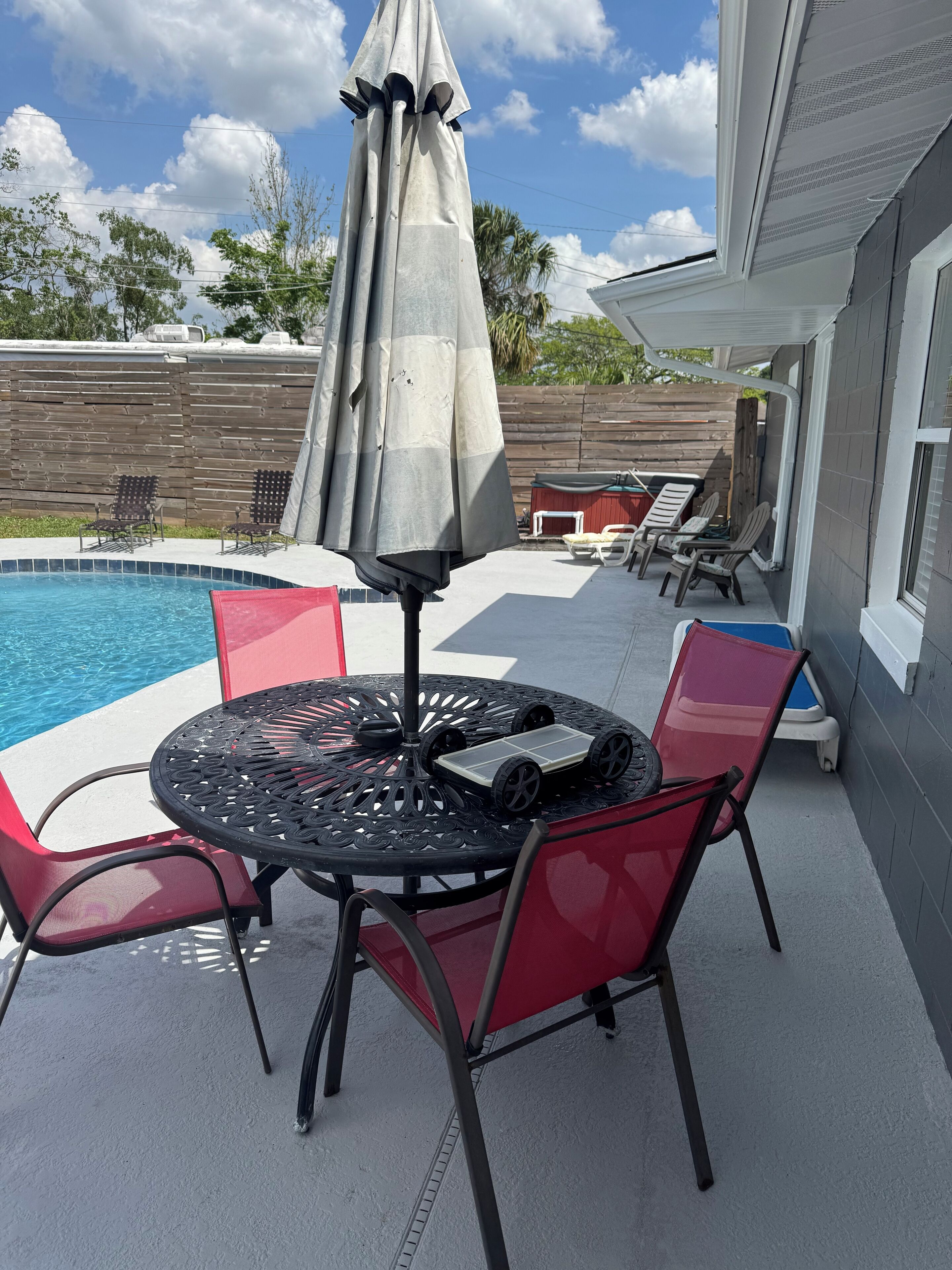 Un patio con piscina, una mesa redonda con sillas y una sombrilla.