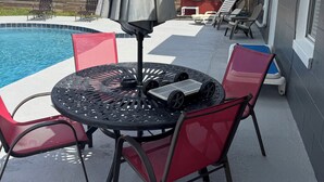 A patio with a pool, a round table with chairs, and an umbrella.