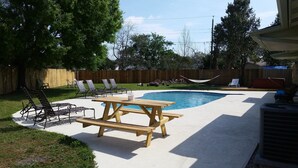 A backyard with a swimming pool, lounge chairs, a picnic table, and a wooden fence.