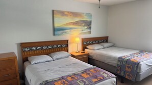 A hotel room with two beds, a nightstand with a lamp, a painting on the wall, and a ceiling fan.