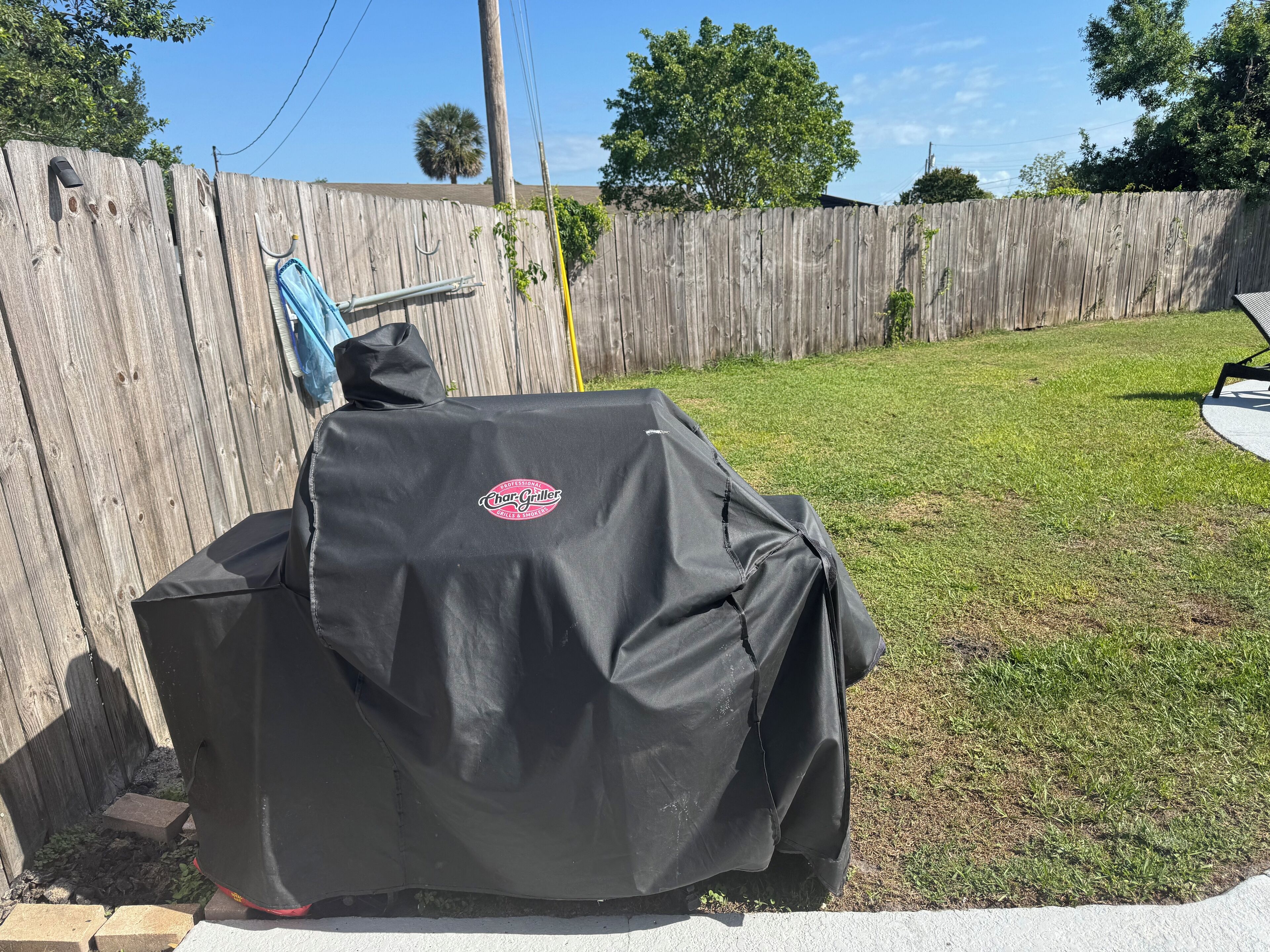 A covered barbecue grill in a backyard with a wooden fence and grass.