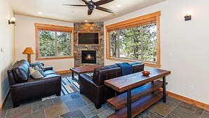 A modern living room with a stone fireplace, leather sofas, a wooden dining table, and large windows.