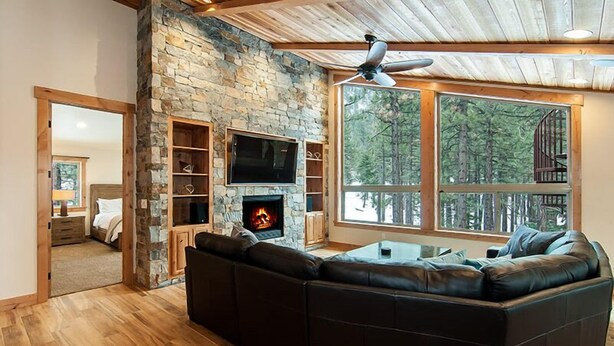 A cozy living room with a stone fireplace, a large black leather sofa, and a television mounted on the stone wall.