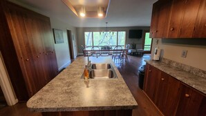 A kitchen with granite countertops, wooden cabinets, a stainless steel sink, and a dining area with chairs and a table. - Private Mohican Riverfront - Popular Location/Loved by Guests (Loudonville)