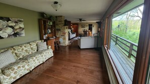 A spacious living area with a wooden floor, a sofa, a dining table, and a kitchen in the background. - Private Mohican Riverfront - Popular Location/Loved by Guests (Loudonville)