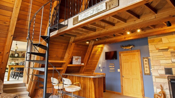 A wooden interior with a spiral staircase, a ceiling fan, a stone fireplace, and a wooden bar area. - Private Mohican Riverfront - Popular Location/Loved by Guests (Loudonville)