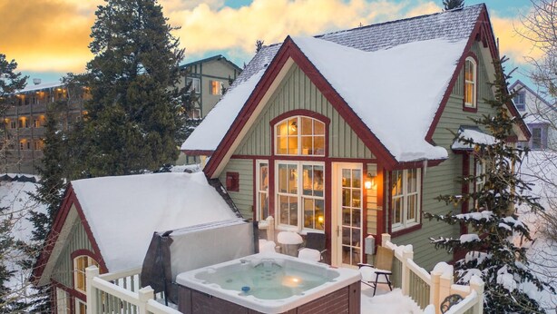 Un cálido chalet con jacuzzi y terraza, rodeado de árboles cubiertos de nieve.