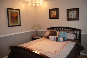 Una cama bien hecha con colcha y almohadas, una lámpara de noche y cuadros en la pared.